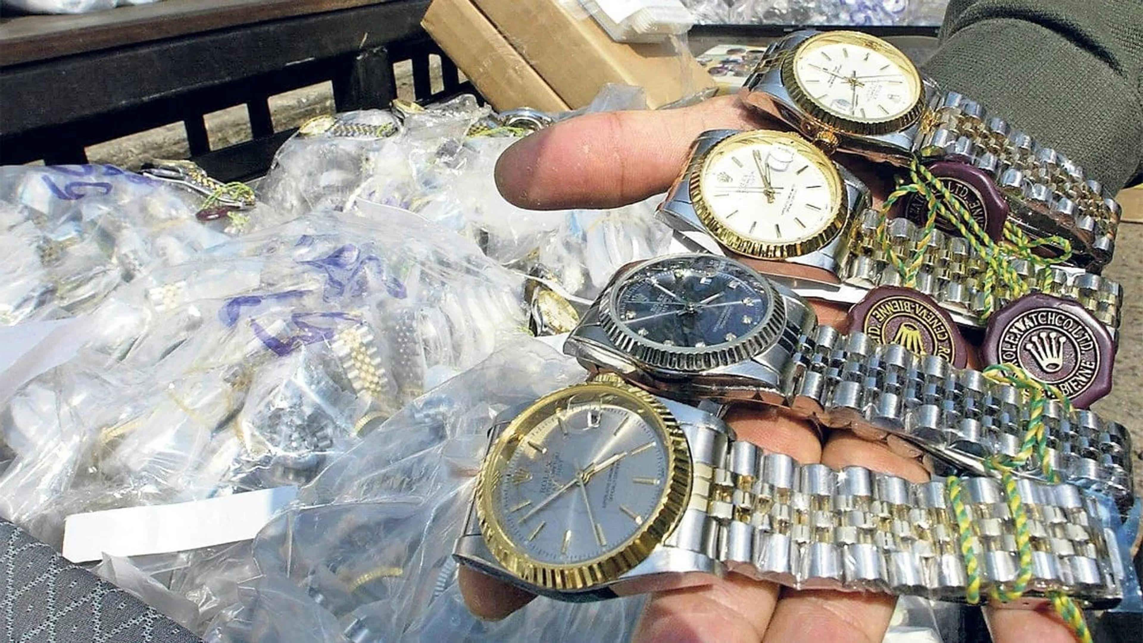 A handful of counterfeit watches beside bags of seized fakes