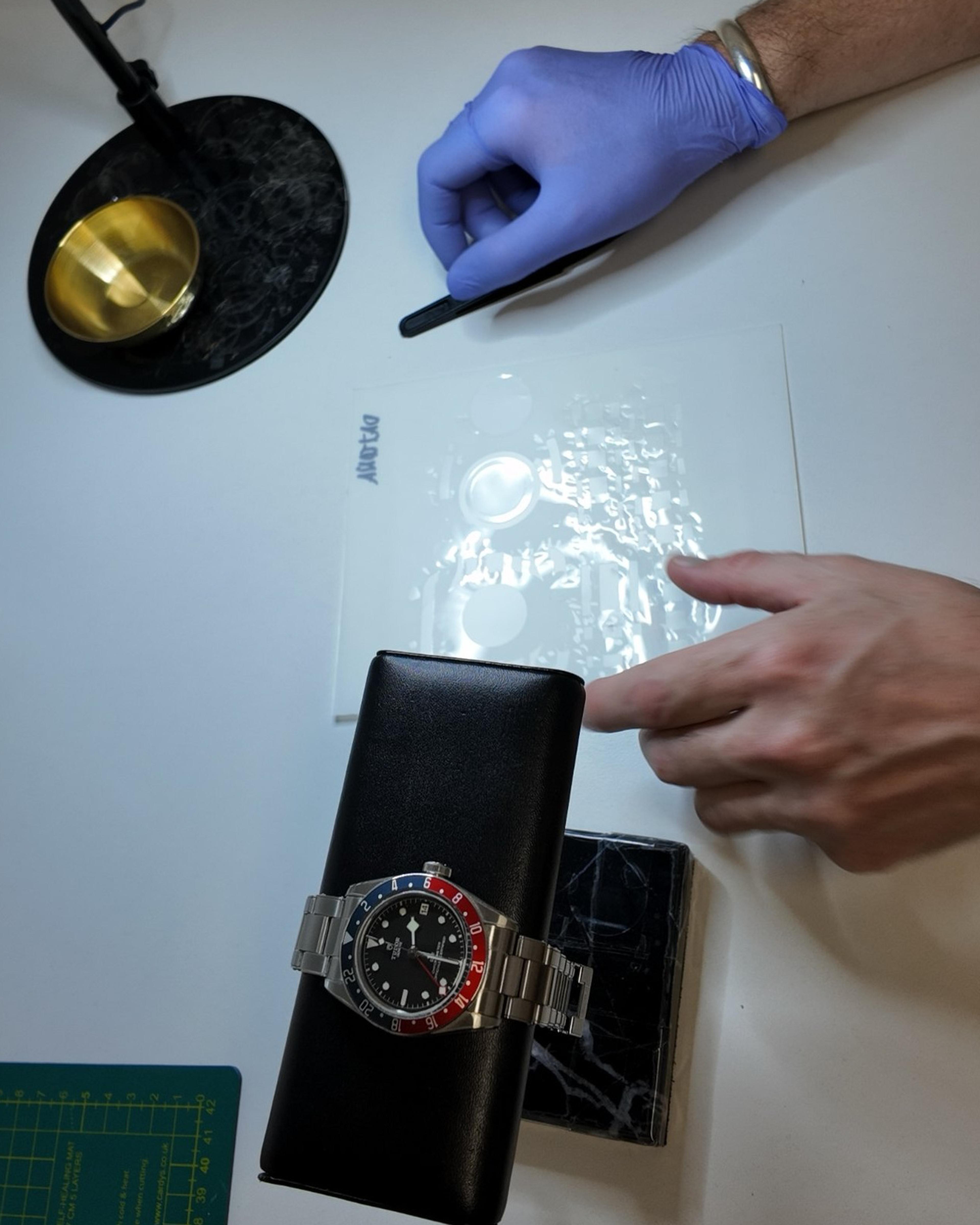 A sheet of film cut to a watch template, laid out on the bench beside the watch