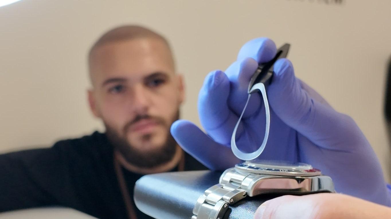 A pre-cut bezel film held with tweezers above a steel watch in the studio