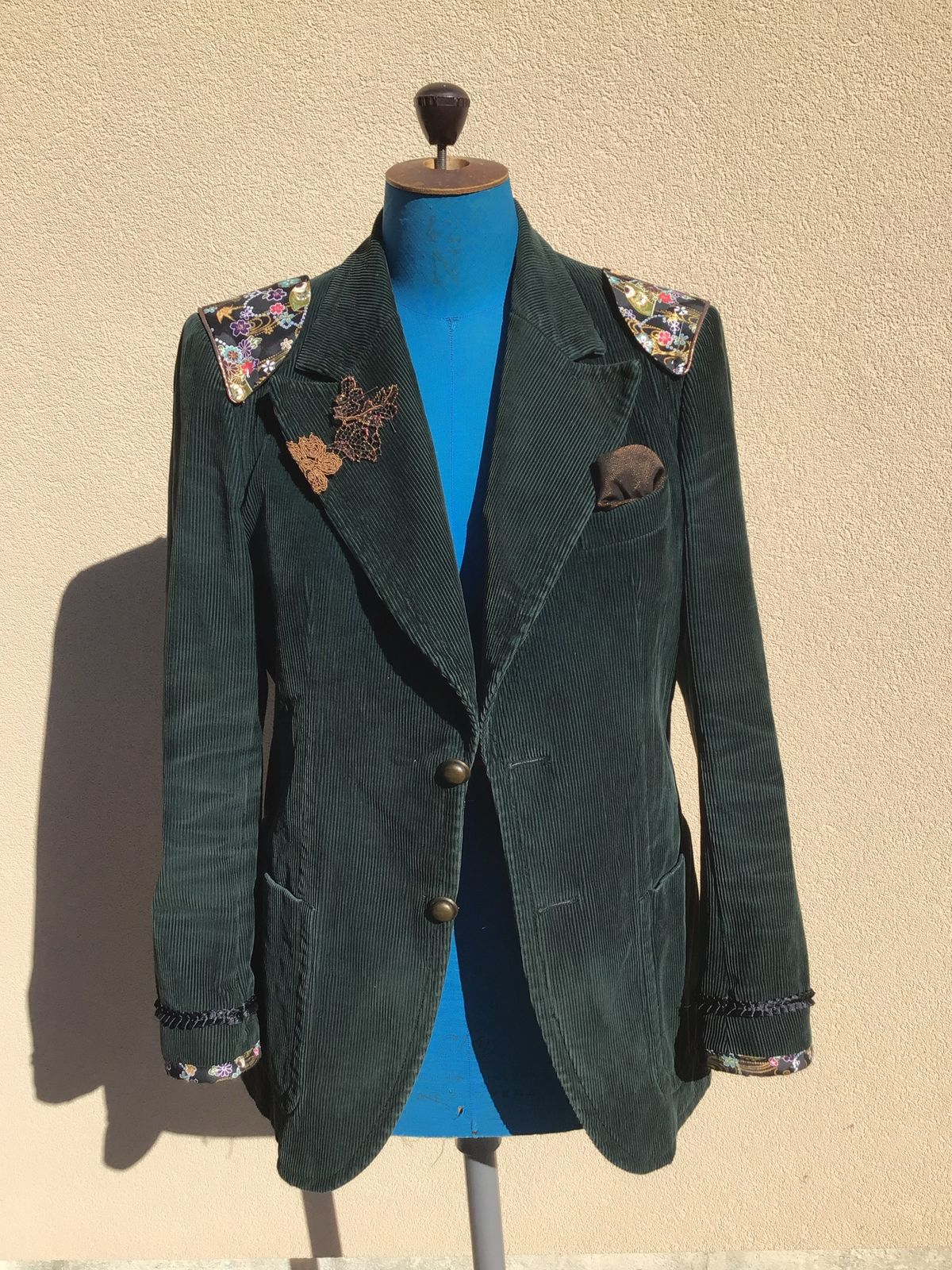 Veste en velours vert sur mannequin, épaulettes en tissu fleuri et broderies sur le revers