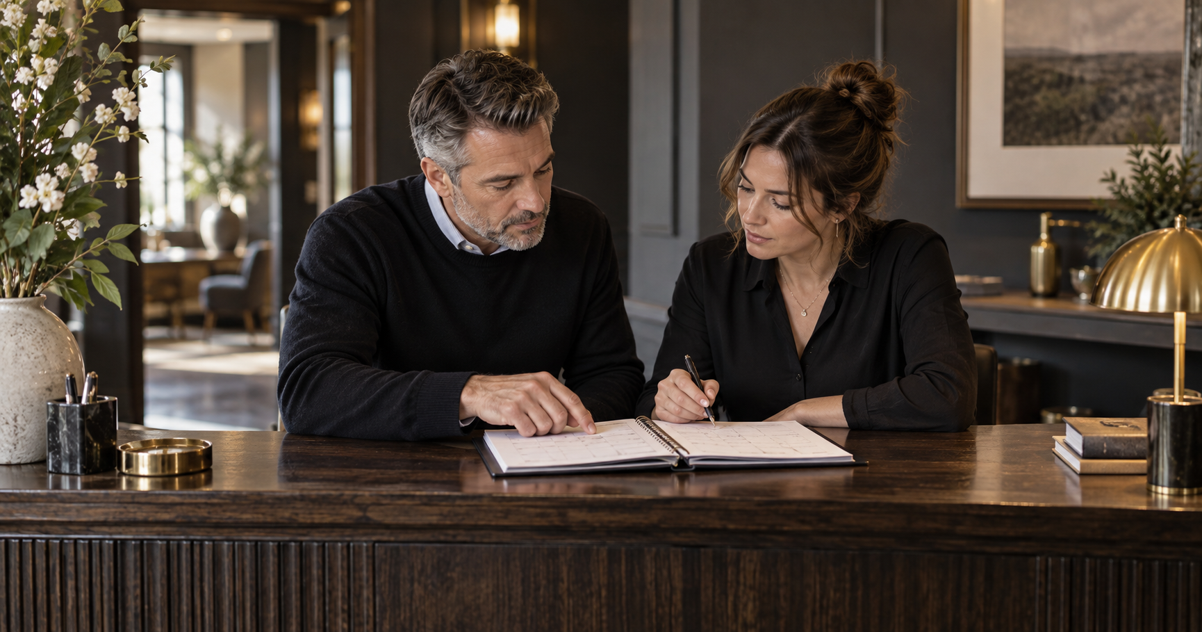 Two colleagues review an appointment planner at a reception desk.