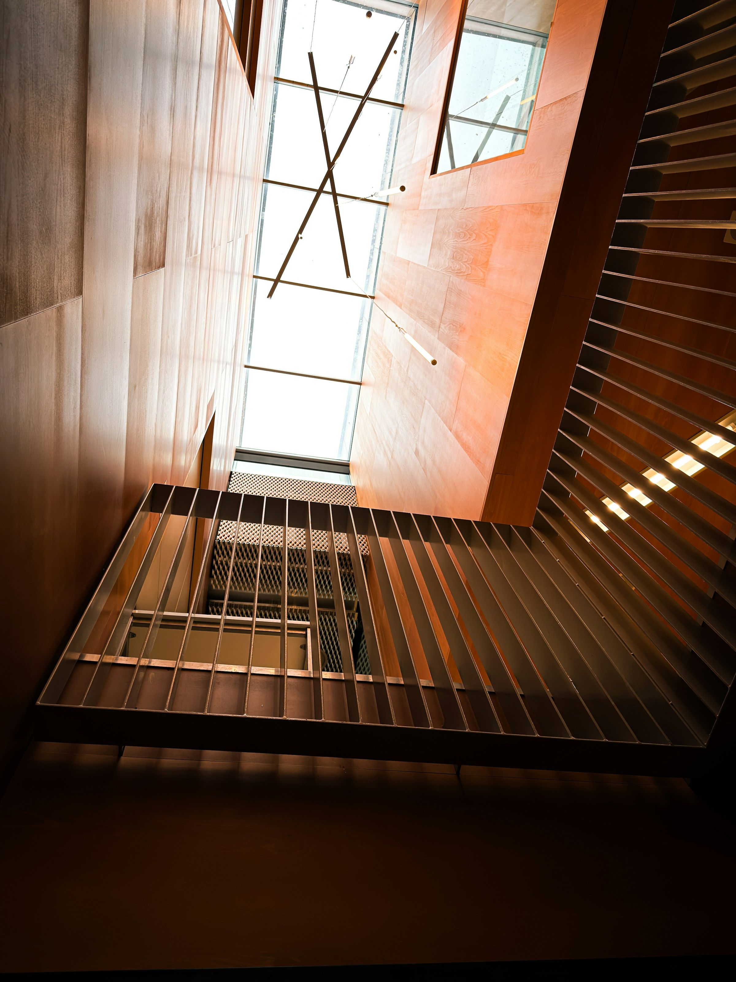 Looking up through a timber-lined staircase toward a skylight.