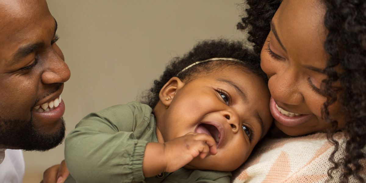 Smiling parents cuddle their laughing baby, sharing a warm and joyful moment together.