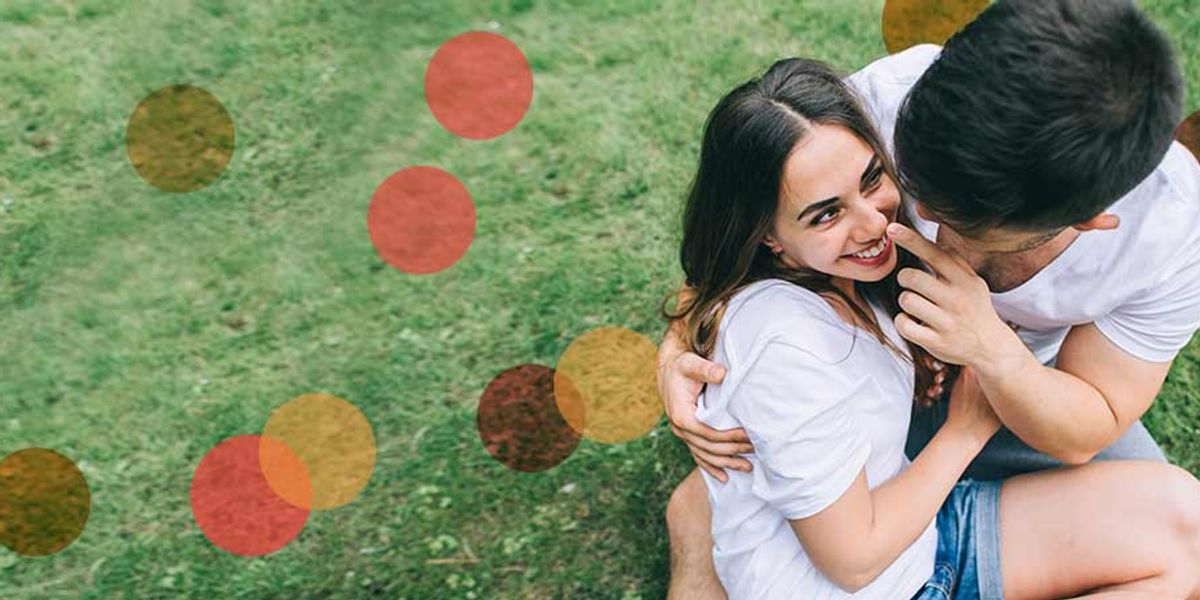 Couple sitting on the grass, laughing and cuddling closely, sharing a playful and affectionate moment outdoors