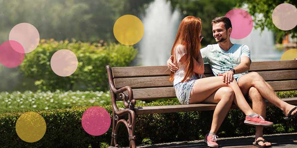 Couple sitting on a park bench near a fountain, smiling and talking closely, with colorful circles overlaid on the image.