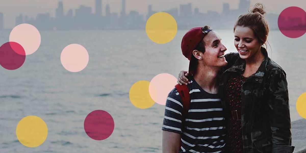 Smiling couple standing by the water at dusk with a city skyline behind them, surrounded by colorful circles overlaid on the image.
