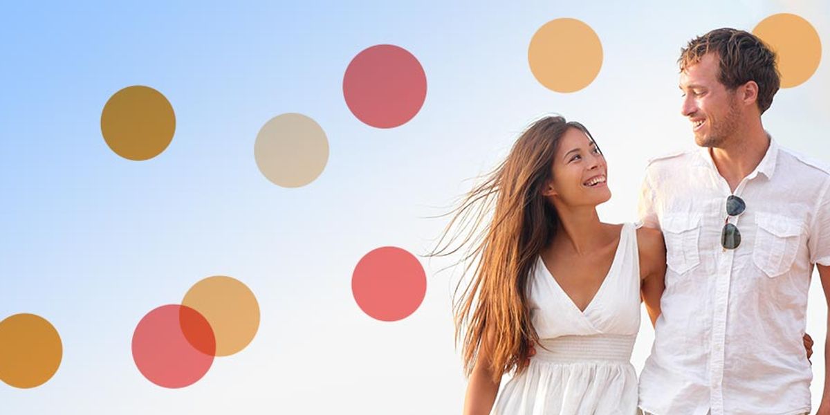 Smiling couple walking together outdoors on a bright day, looking at each other warmly