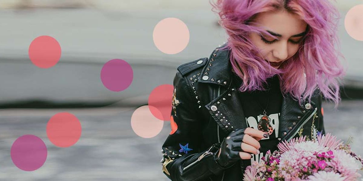 Young woman with pink hair in a studded leather jacket looks down at a bouquet of flowers