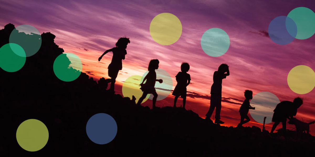 Silhouettes of children running and playing on a hill at sunset against a colorful sky.