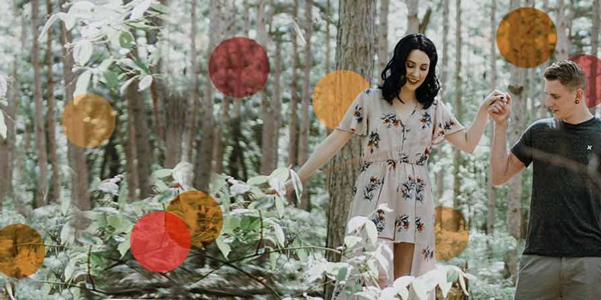 Couple walking hand in hand through a forest, smiling as they balance together on a fallen log.