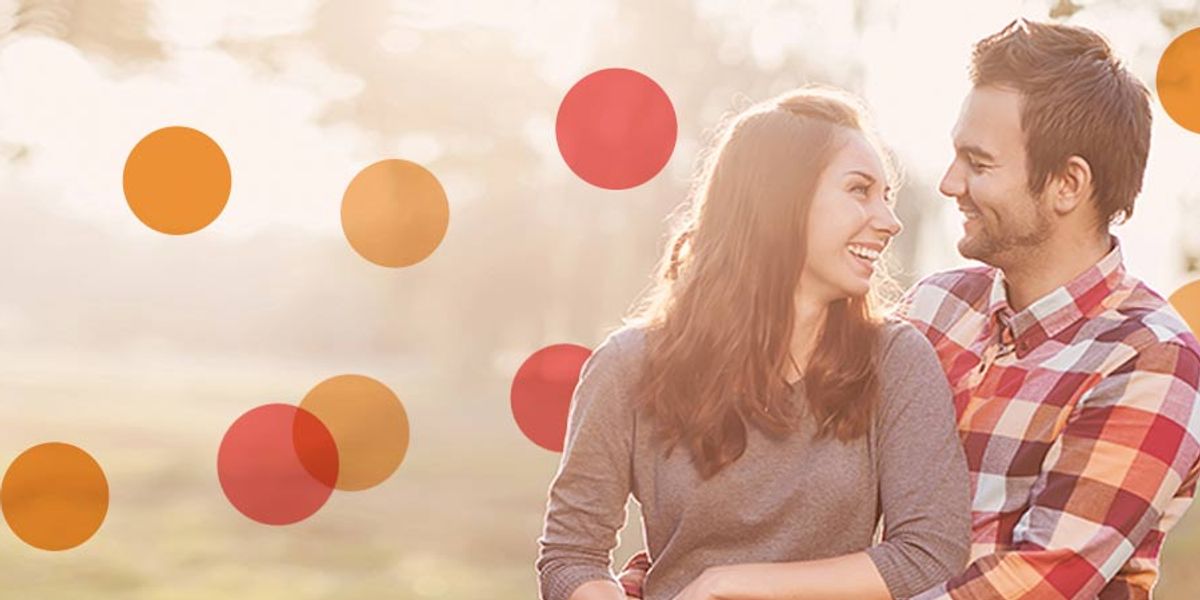 Smiling couple sitting together outdoors in warm sunlight, looking at each other with affection.