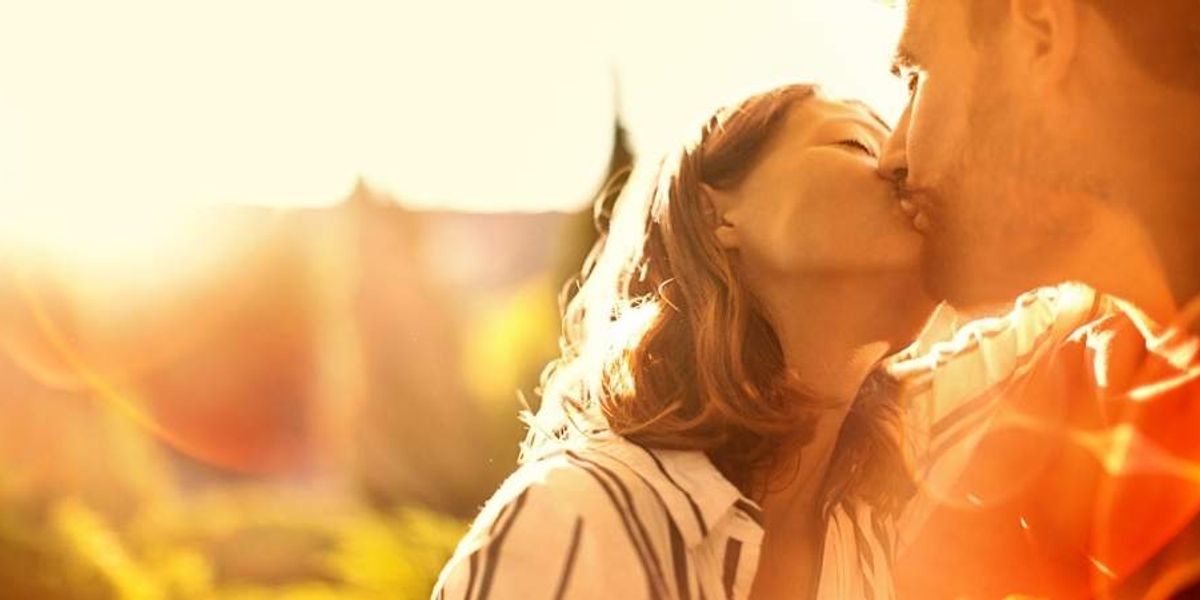 Couple sharing a gentle kiss in warm golden sunlight, surrounded by a soft, glowing outdoor backdrop.