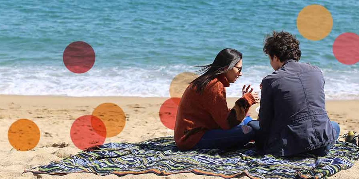 Couple sitting on a blanket at the beach, talking by the shoreline