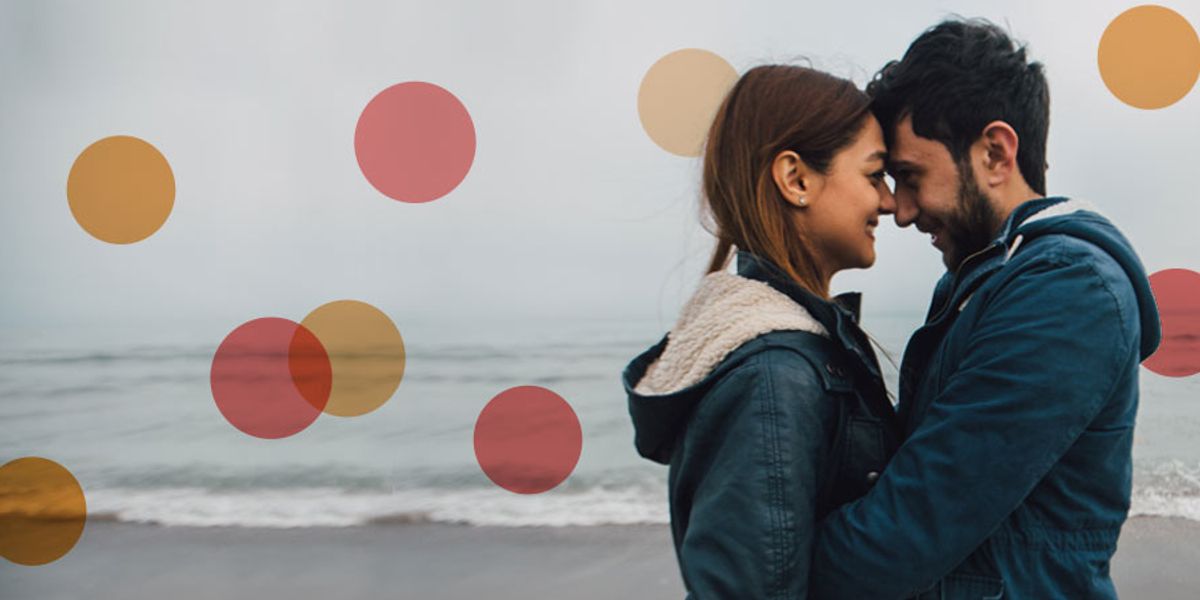 Couple standing close together on a cloudy beach, touching foreheads and smiling softly