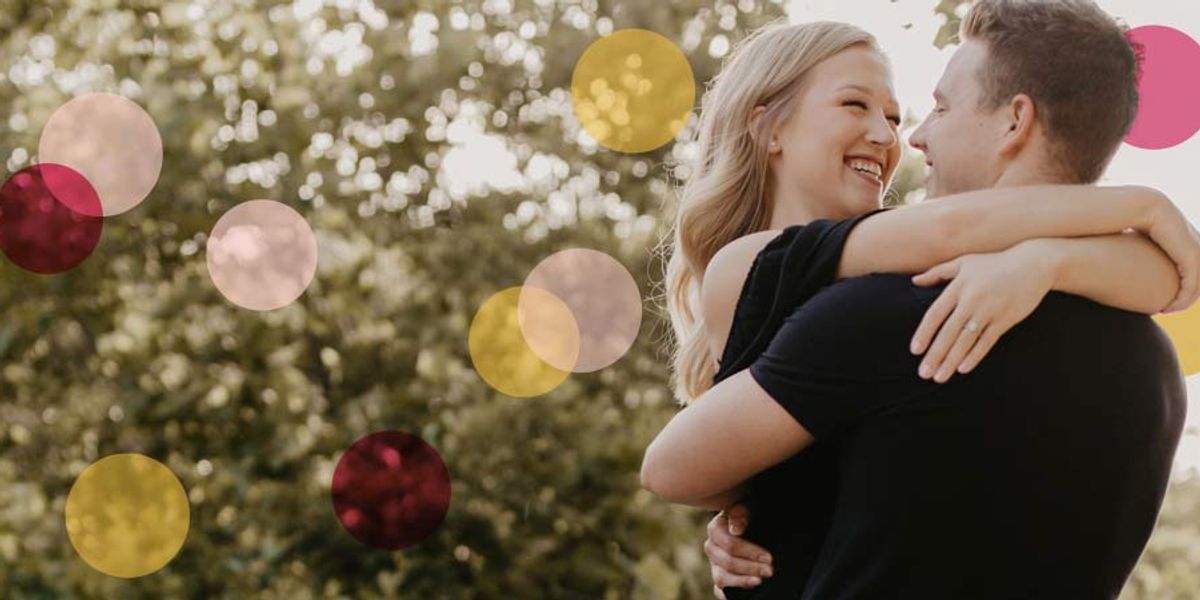 Smiling couple embracing outdoors as the man lifts the woman in his arms, with colorful circles overlaid on the sunlit background.
