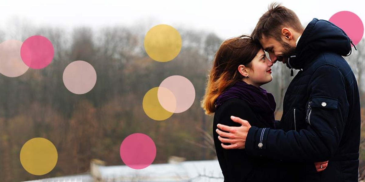 Couple standing close together outdoors on a cold, misty day, touching foreheads and holding each other as soft pink and yellow circles are overlaid on the image.