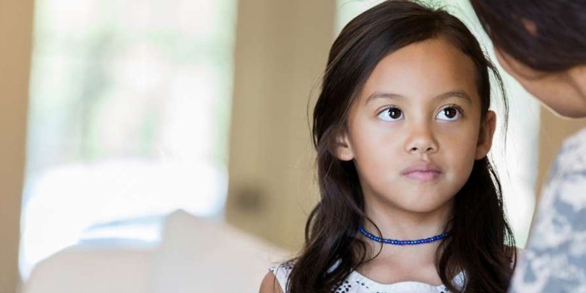 Young girl looking up thoughtfully while an adult speaks to her in a softly lit room.