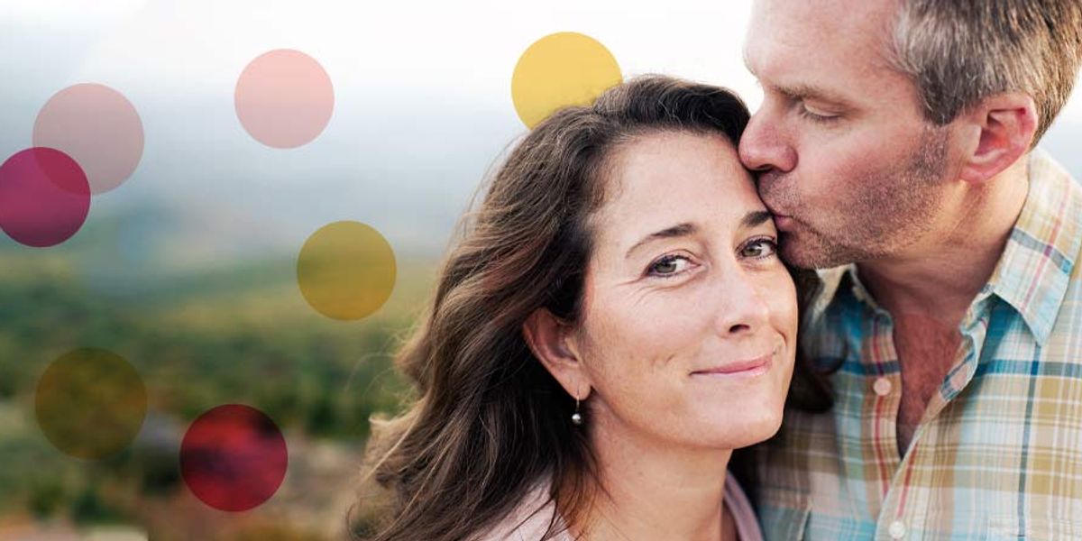 Man kissing a woman on the forehead as she smiles softly at the camera, with colorful circles overlaid on a blurred outdoor background.