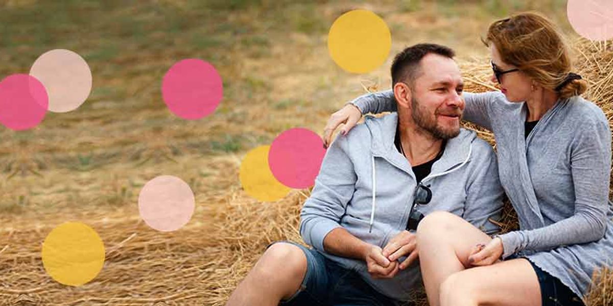 Couple sitting close on hay in a field, smiling warmly at each other with soft pink and yellow circle overlays.