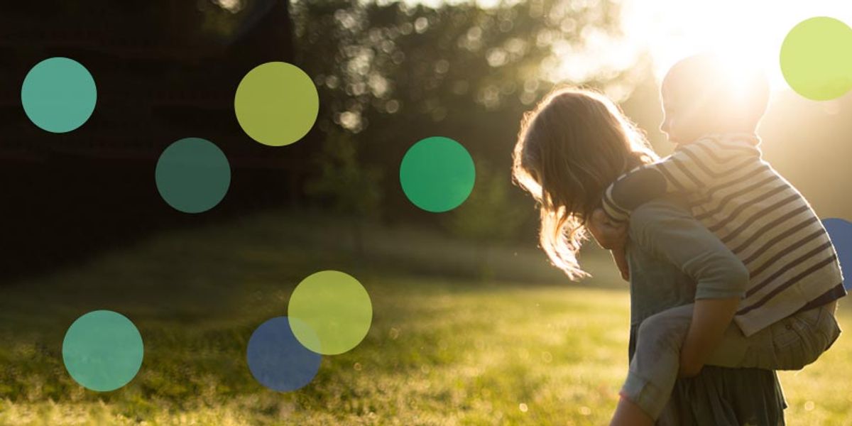 Smiling child riding piggyback on an adult in a sunlit field with soft, glowing light behind them.