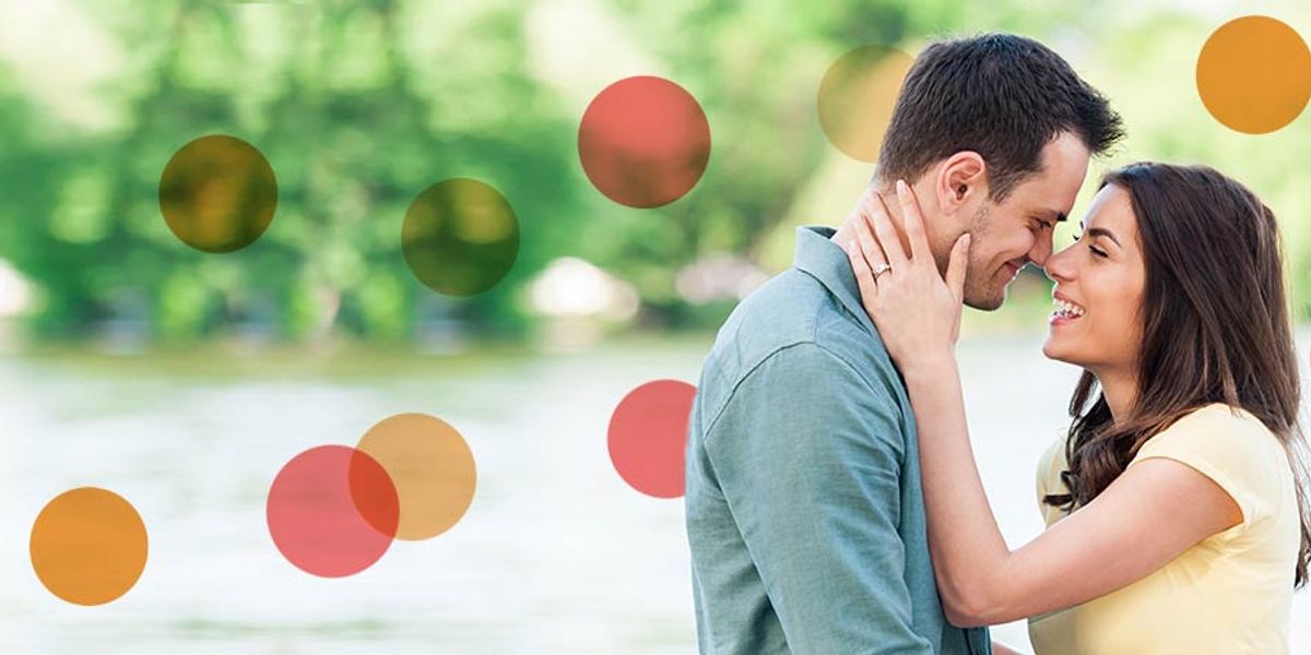 Smiling couple touching foreheads by the water on a sunny day, sharing an affectionate moment
