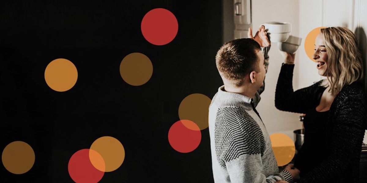 Couple smiling and talking in a cozy kitchen as they hold mugs