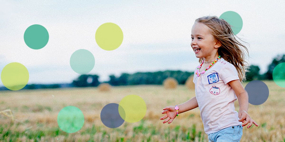 Smiling young girl running through a field on a breezy day, wearing a pink shirt and colorful jewelry.