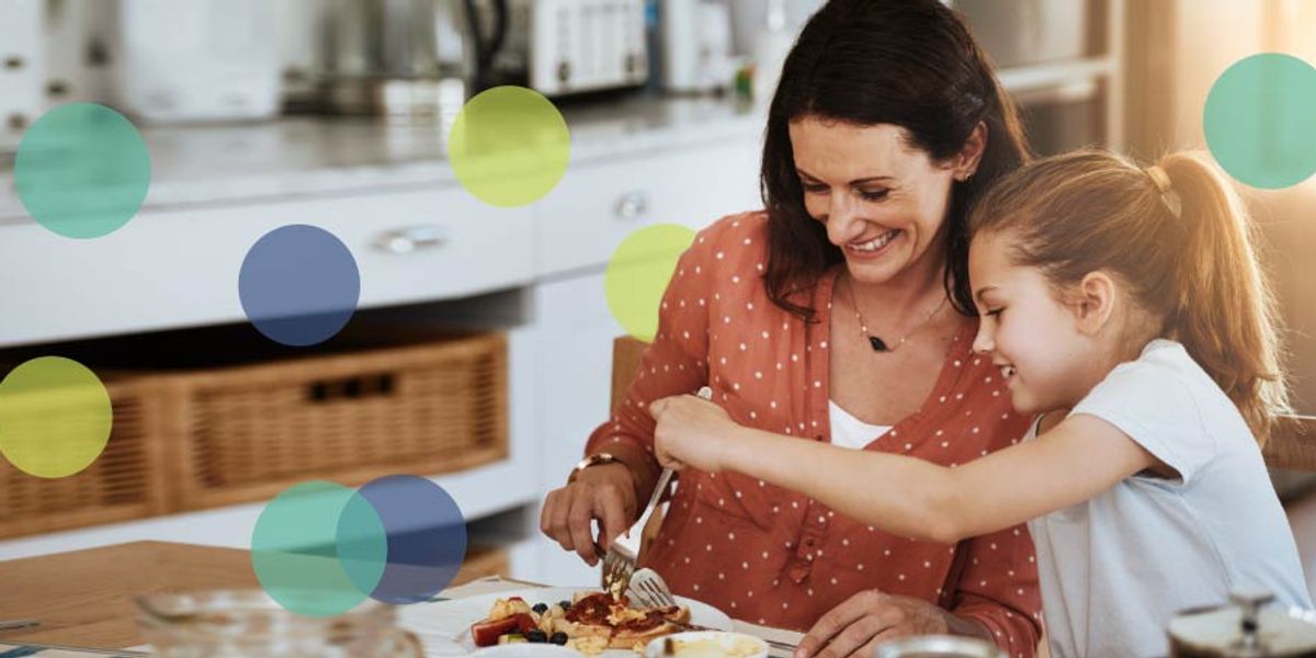 Mother and daughter smiling while sharing breakfast at the kitchen table, with soft colorful circles over the image.