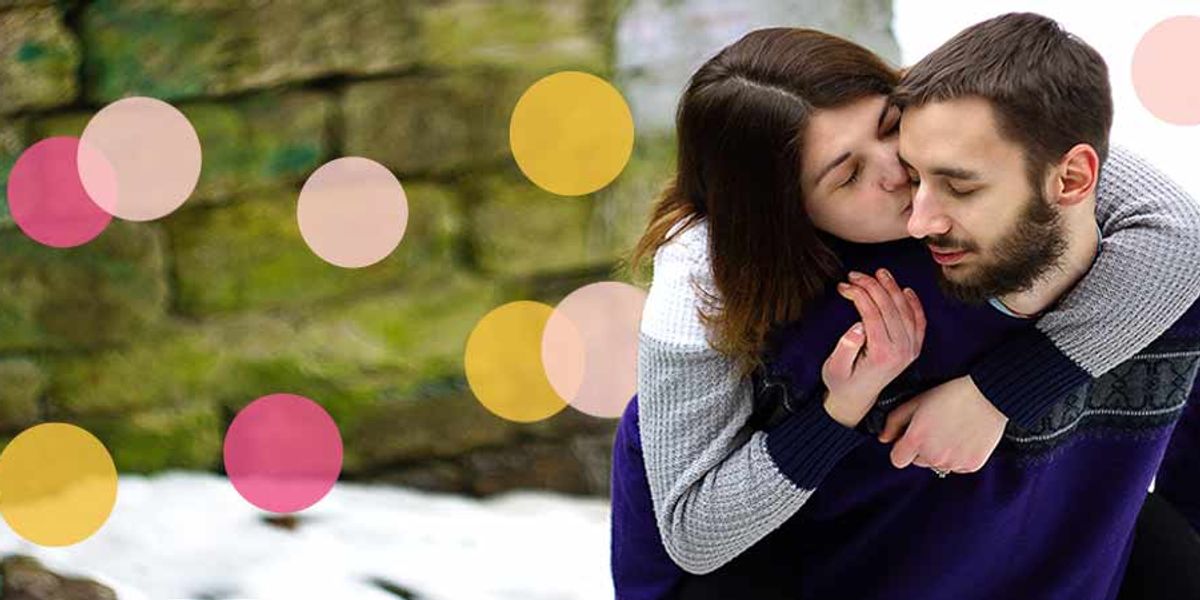 Woman playfully kissing a man’s cheek while riding on his back in a snowy outdoor setting, with soft pink and yellow circles overlaid on the image.