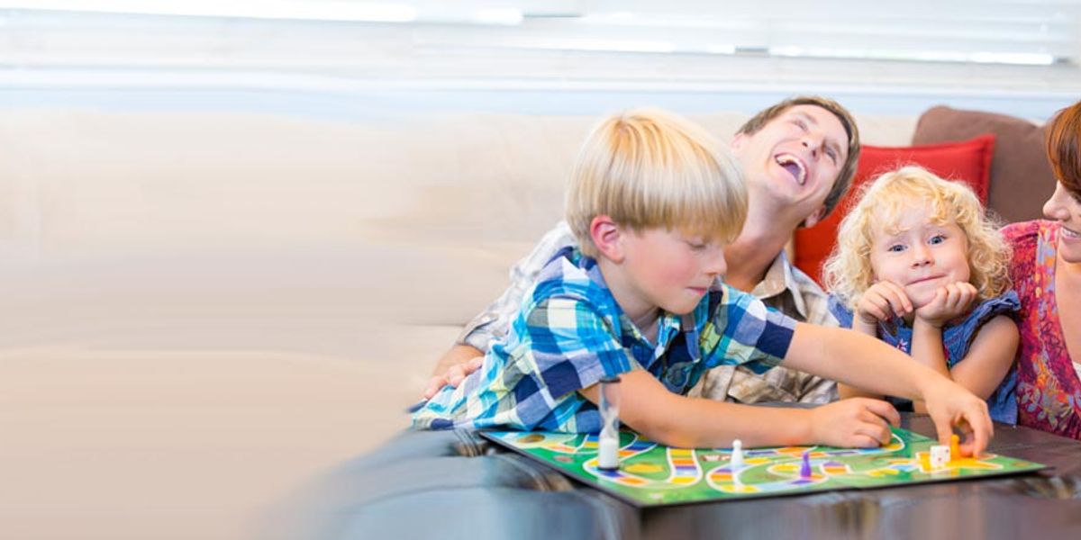 Family sitting on the couch playing a colorful board game together, laughing and enjoying the moment.