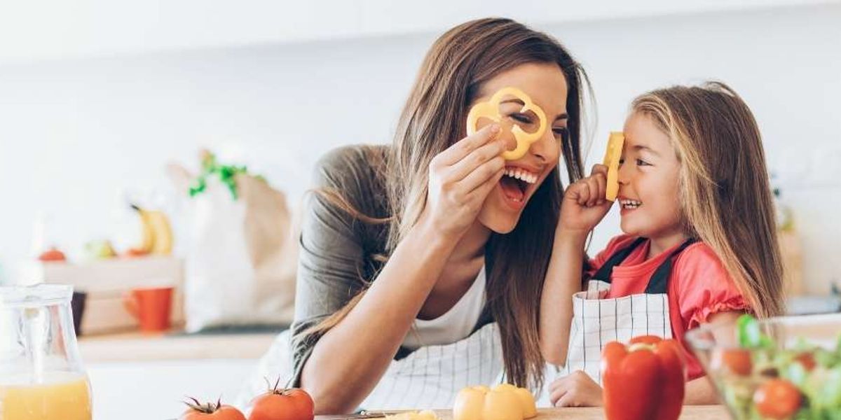 Mother and daughter playfully hold pepper slices over their eyes while cooking together in the kitchen.