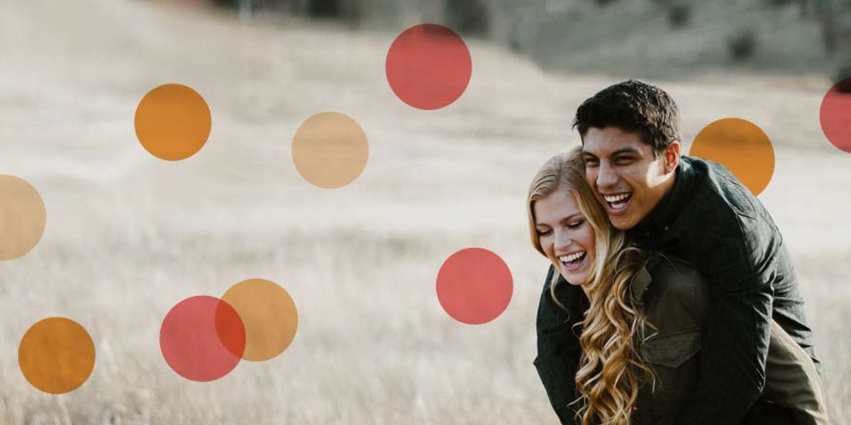 Laughing couple outdoors, with the man giving the woman a playful piggyback ride in a field