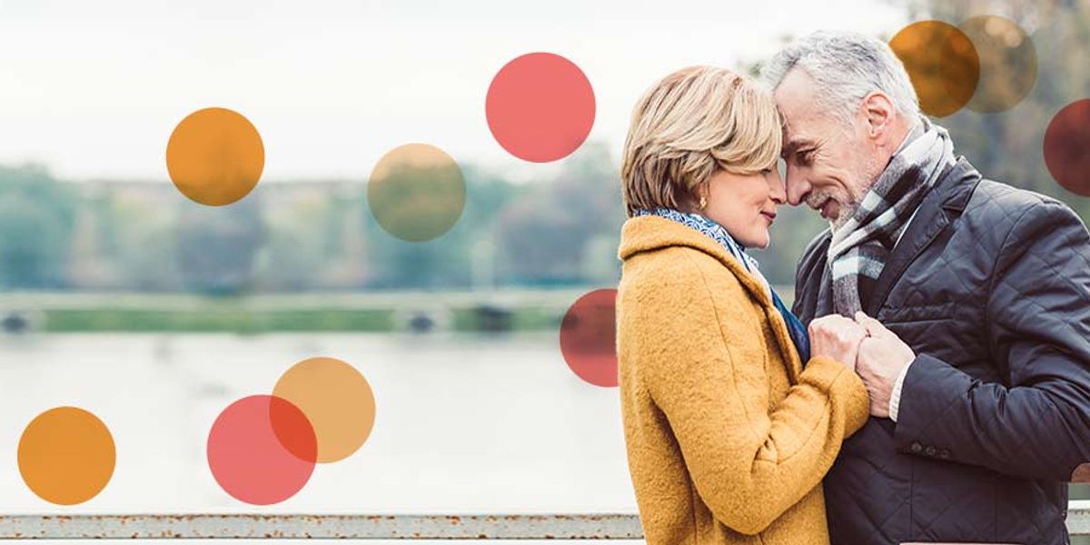 Older couple standing close by the water, holding hands and touching foreheads