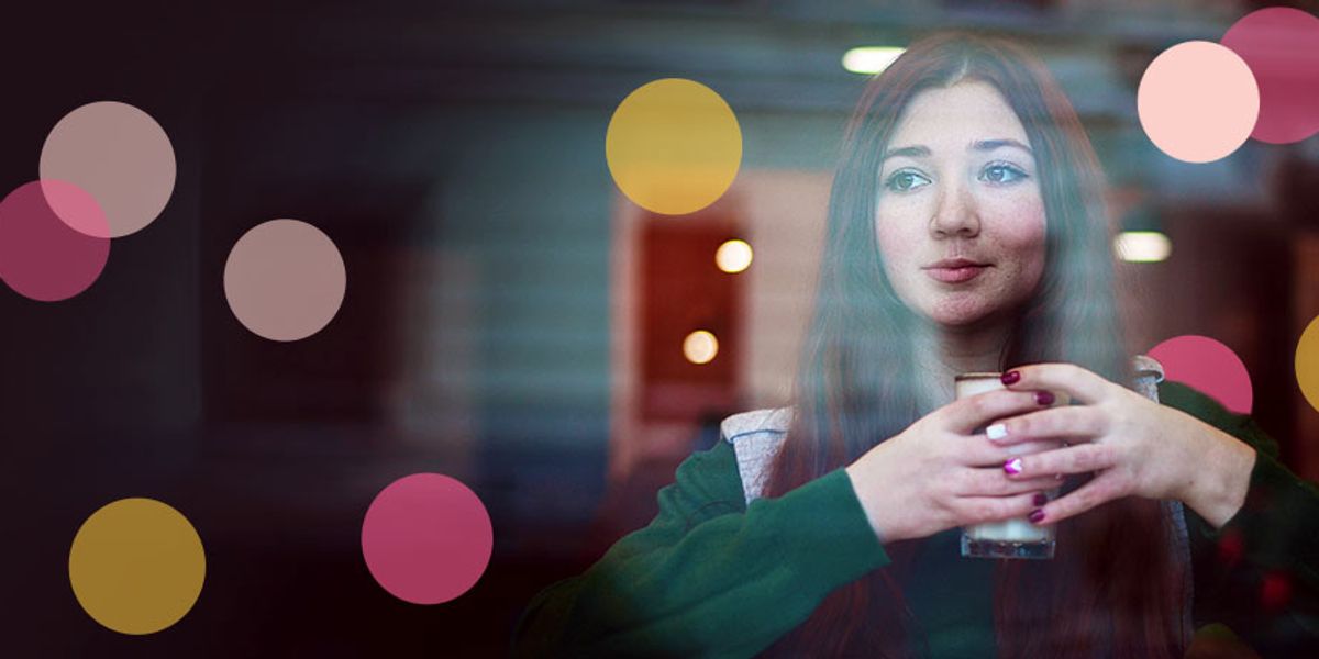 Woman with long red hair holding a cup and gazing thoughtfully through a window, with colorful soft-focus circles overlaying the scene.