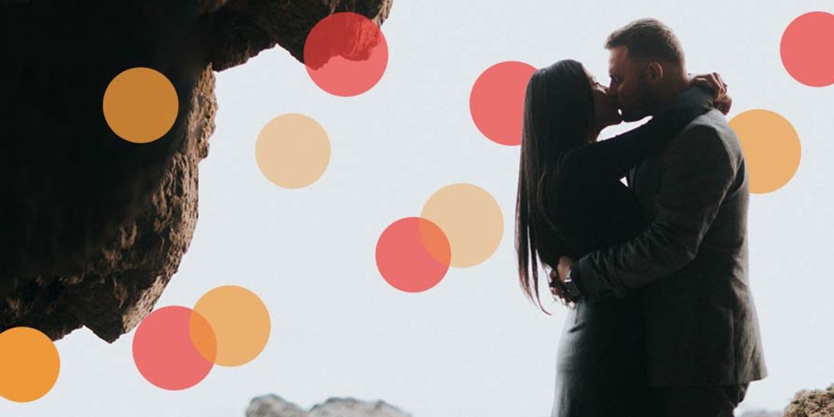 Couple kissing while standing together near rocky cliffs, sharing an intimate moment