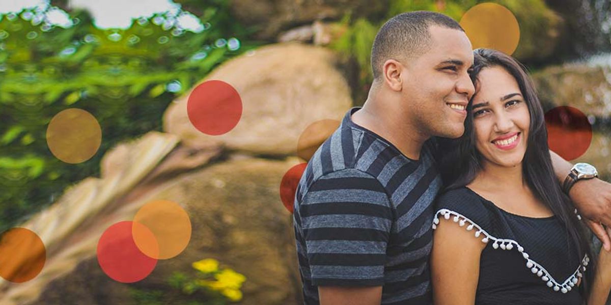 Couple standing together outdoors, smiling and embracing near rocks and greenery