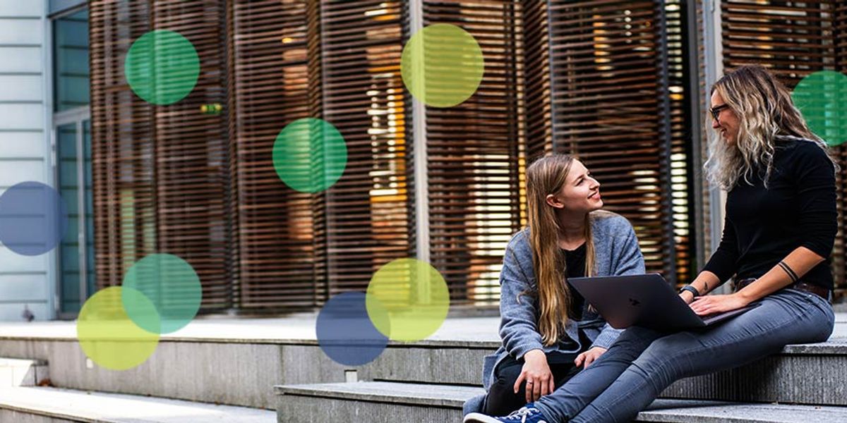 Mother and teen daughter sitting on outdoor steps, smiling and talking while using a laptop together.