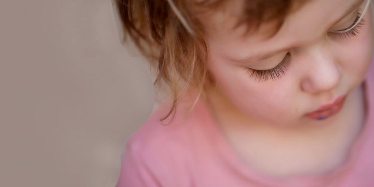 Close-up of a young child looking down quietly, with long eyelashes and soft lighting on their face.