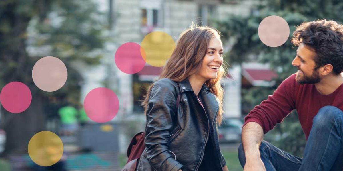 Smiling couple sitting outdoors and talking, with soft pink and yellow confetti-style circles overlaid on the image.