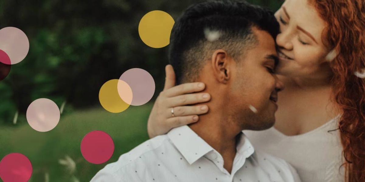 Woman gently embracing and kissing a man’s cheek as he smiles with his eyes closed, with colorful circles overlaid on the soft outdoor background.