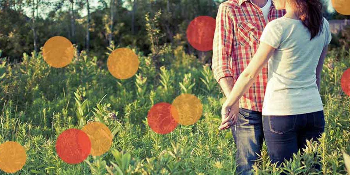 Couple holding hands in a sunlit field, standing close together among tall green plants
