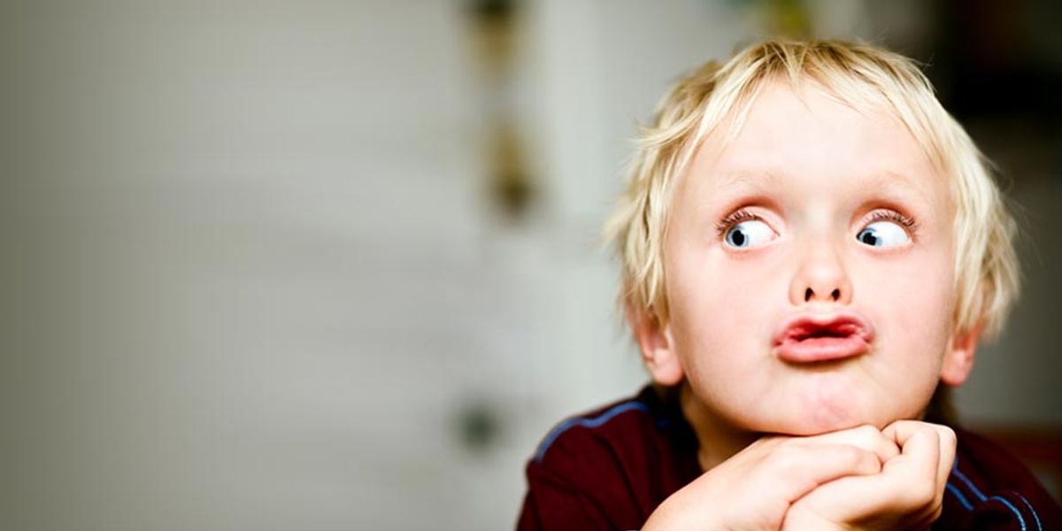 Playful child making a silly face with wide eyes and puckered lips, leaning on folded hands.