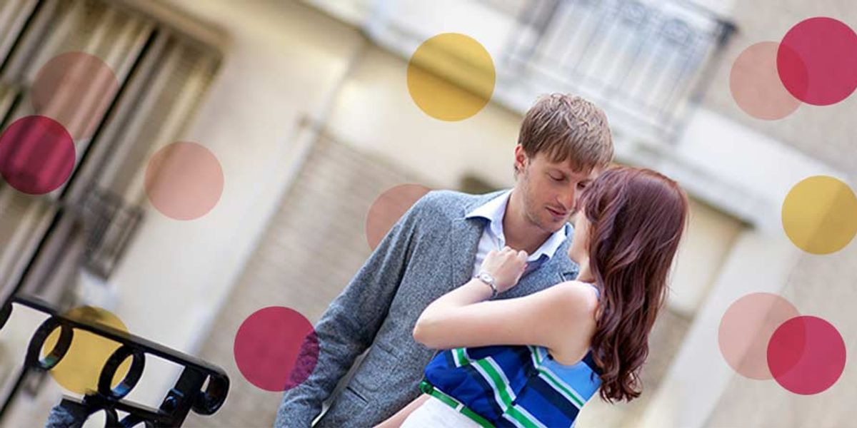Couple sharing a tender moment on a city street, standing close and smiling with soft pink and yellow circles overlaid.