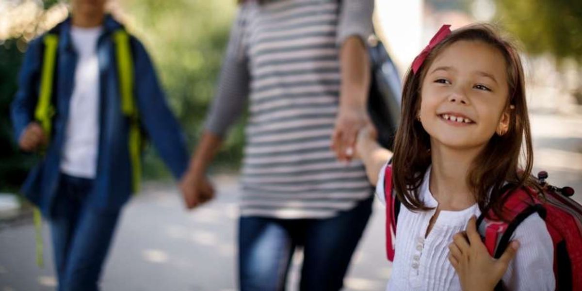 Smiling young girl with a backpack walks beside her family on a sunny day, looking excited.