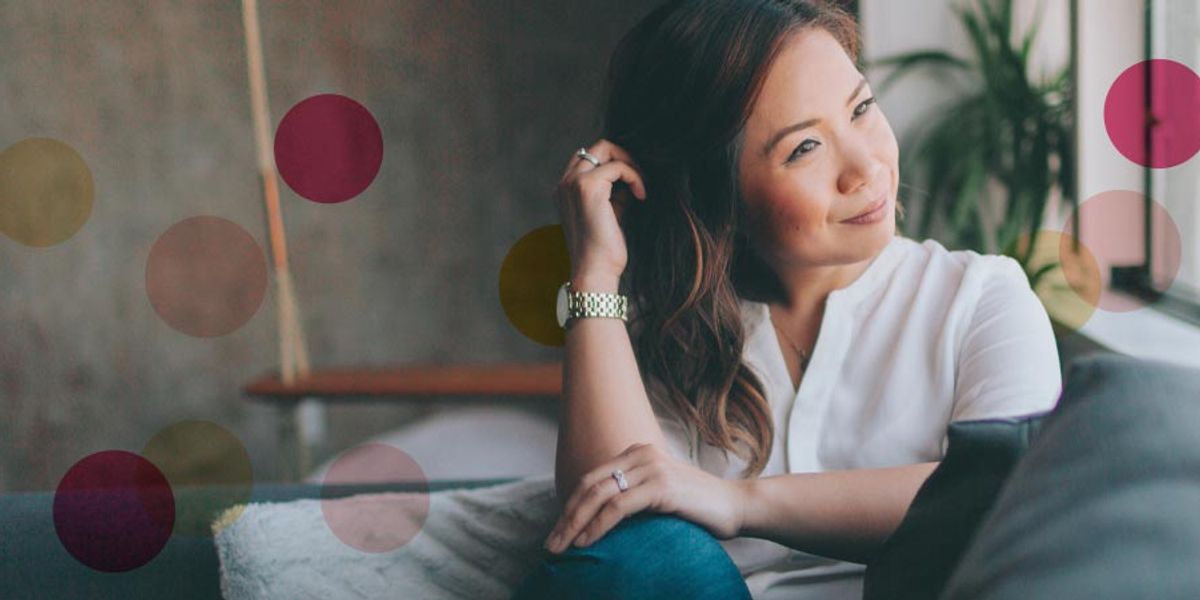 Woman sitting on a couch near a window, smiling softly and looking outside, with colorful circles overlaid on the image.