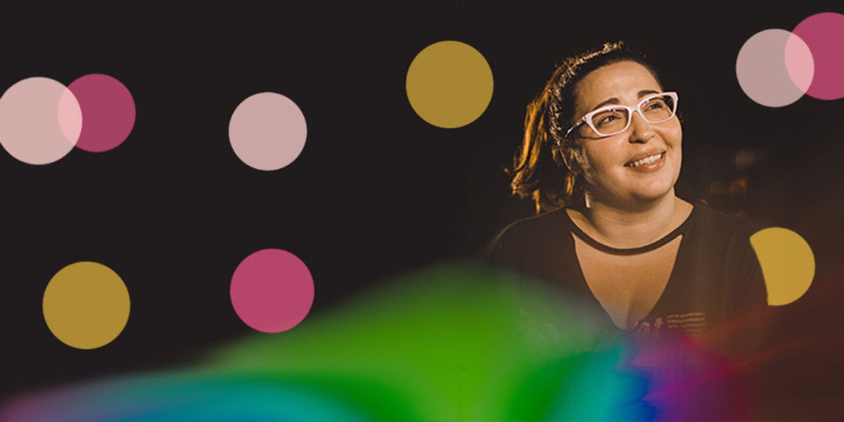 Woman wearing glasses smiling softly in a dark setting with colorful light reflections and soft pink and yellow circles overlaid on the image.