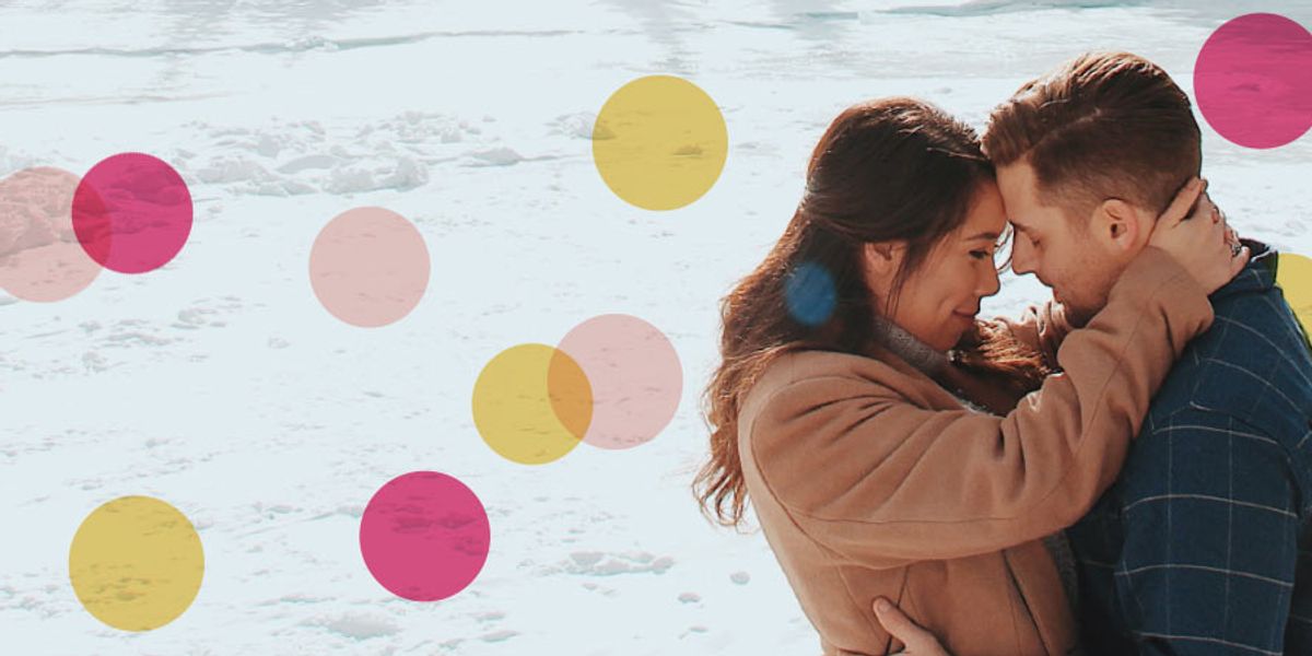 Couple embracing closely in a snowy landscape with their foreheads touching, surrounded by soft pink and yellow circles overlaid on the image.