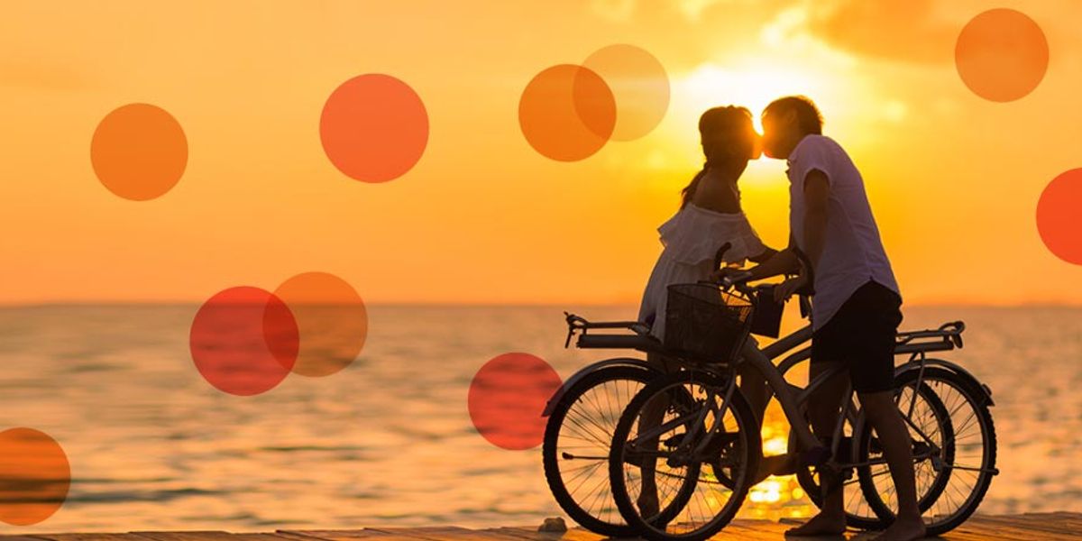 Couple kissing at sunset while standing with their bicycles by the water