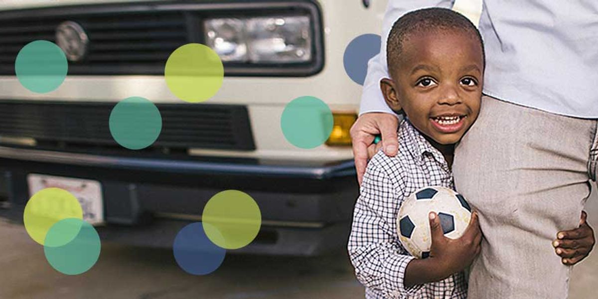 Smiling young boy holding a soccer ball while standing close to an adult beside a parked van.