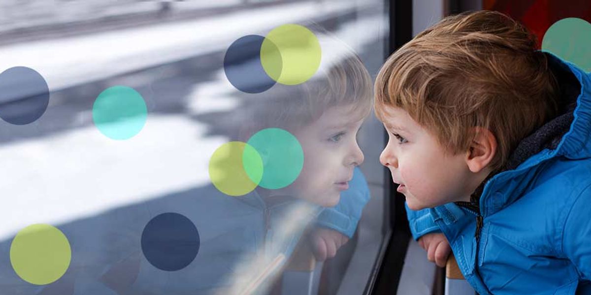 Little boy in a blue jacket gazing out a window, his reflection visible in the glass.